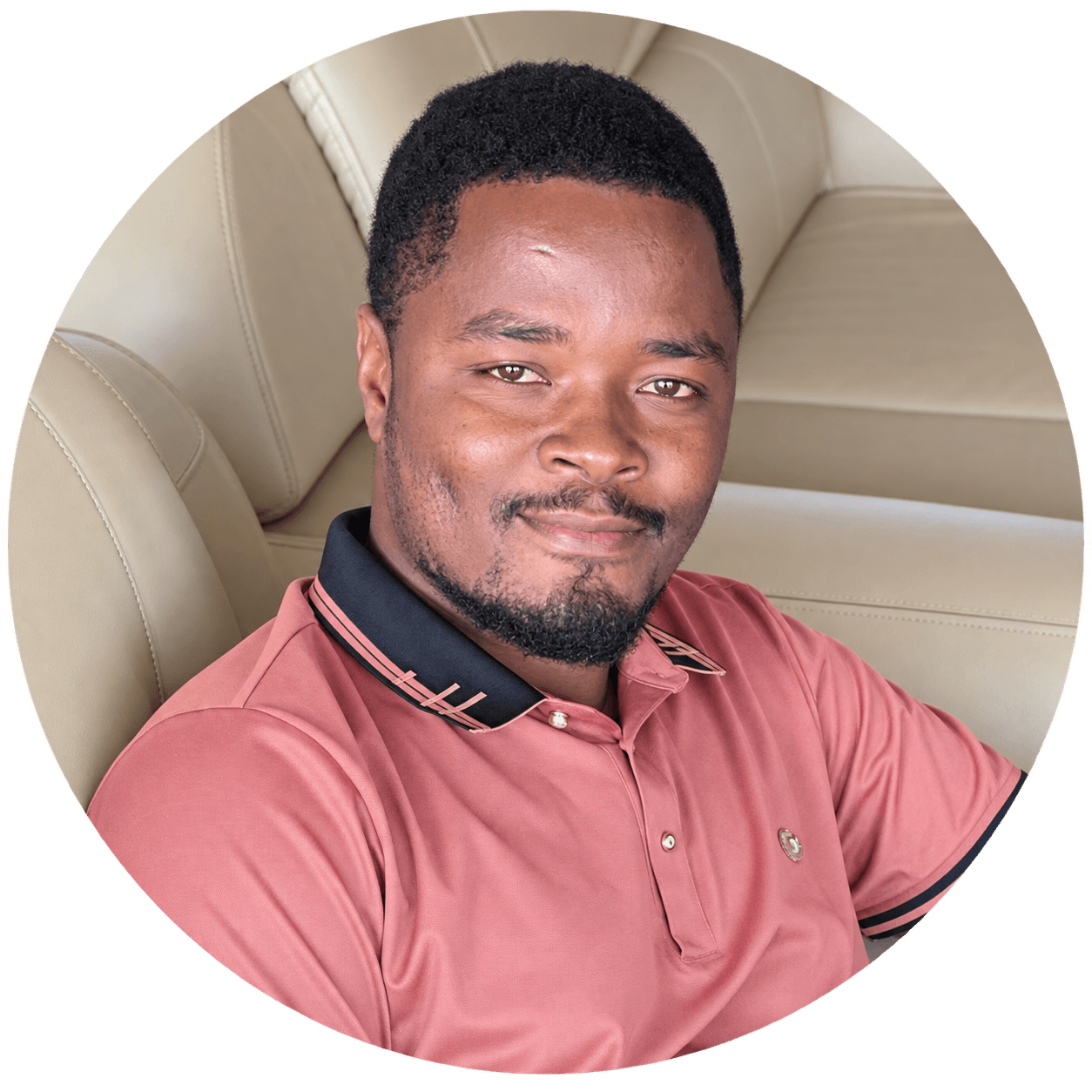Smiling Black man with a beard wearing a pink polo shirt sitting on a couch.